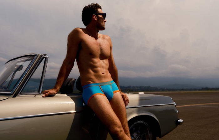 Lifestyle editorial image featuring a male model wearing Cocksox CX68N Apex Collection men's underwear trunks in Capri while leaning against a classic car
